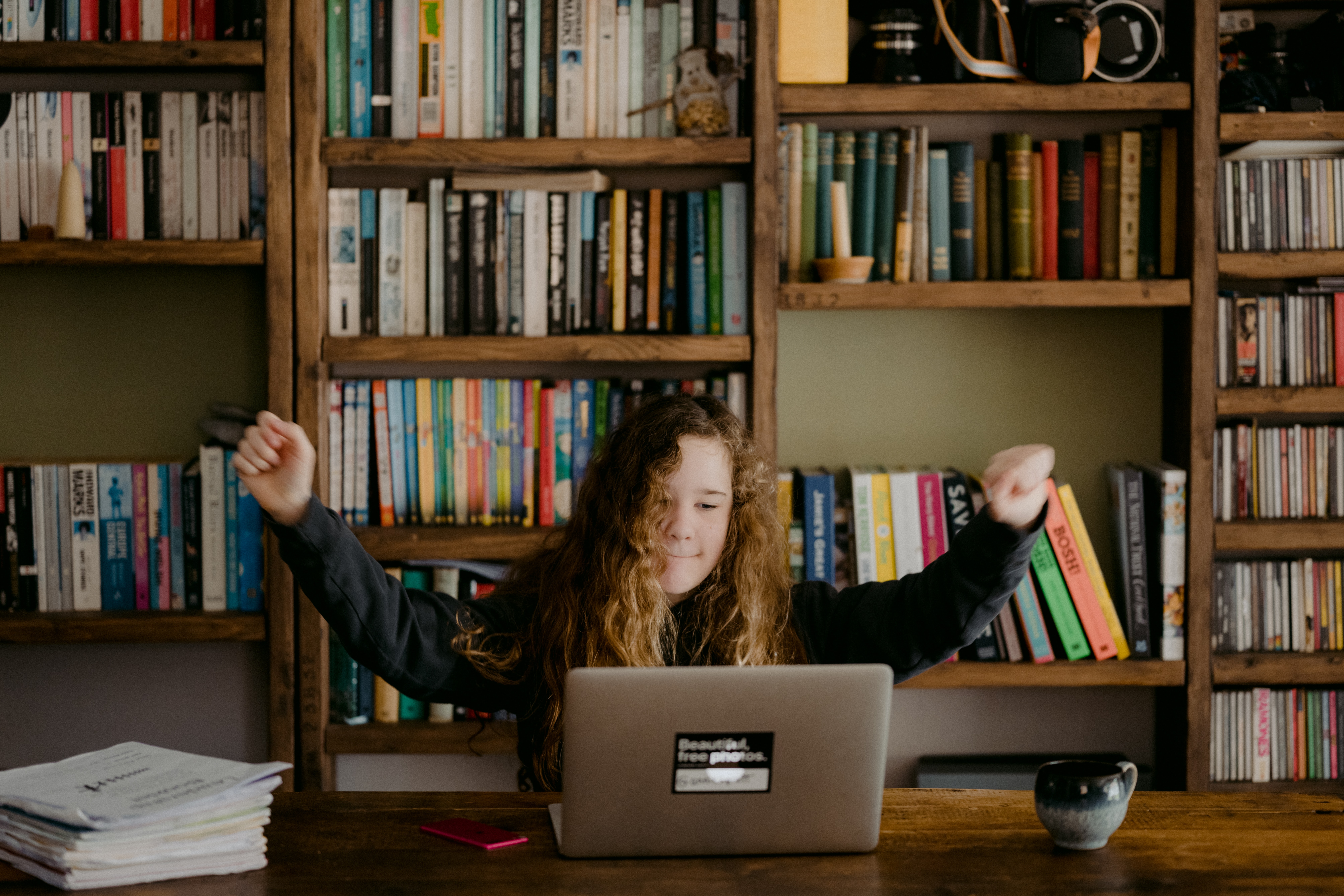 Girl with long hair on computer with shelves of books in background